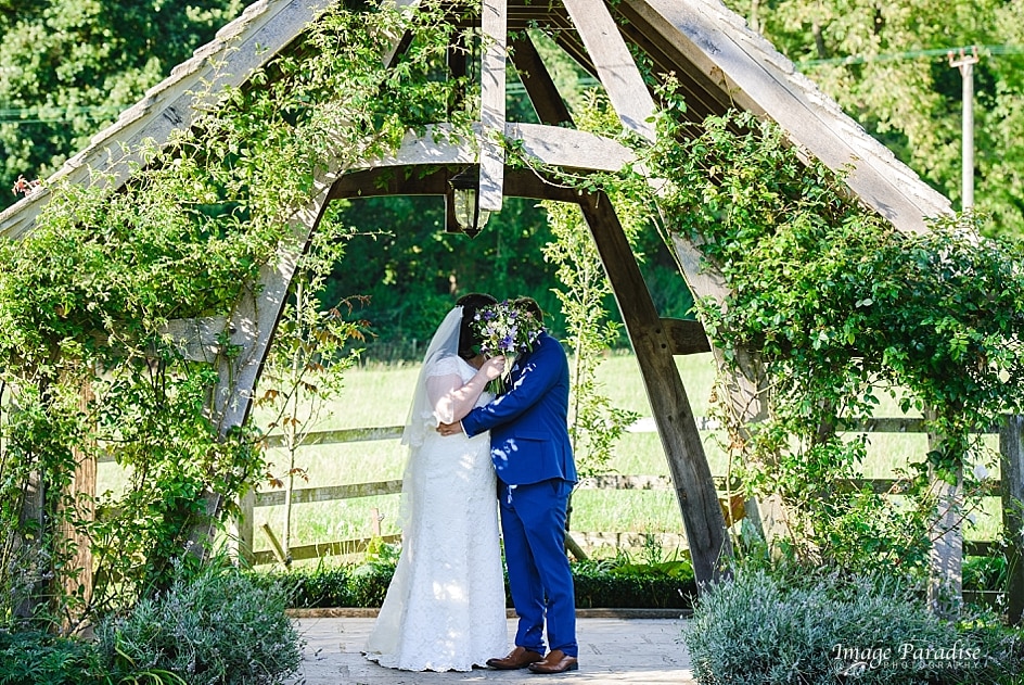 Hyde Barn wedding Cotswolds 17 Bride and groom hiding behind flowers