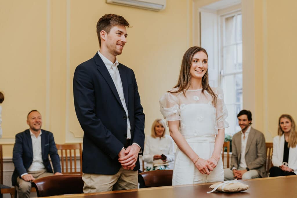 Intimate wedding photography Bristol registry office 14 Couple stood behind the table during their wedding ceremony at the Bristol Room in the registry office Bristol.