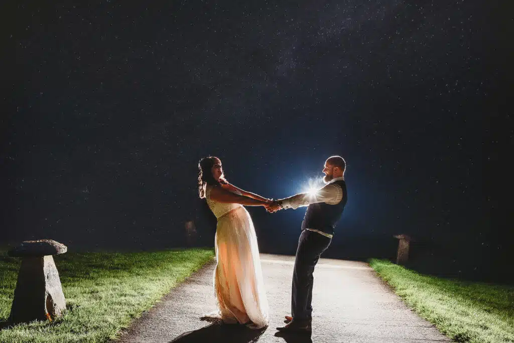 A couple dance on a path at Aldwick Court farm at night backlit with stars