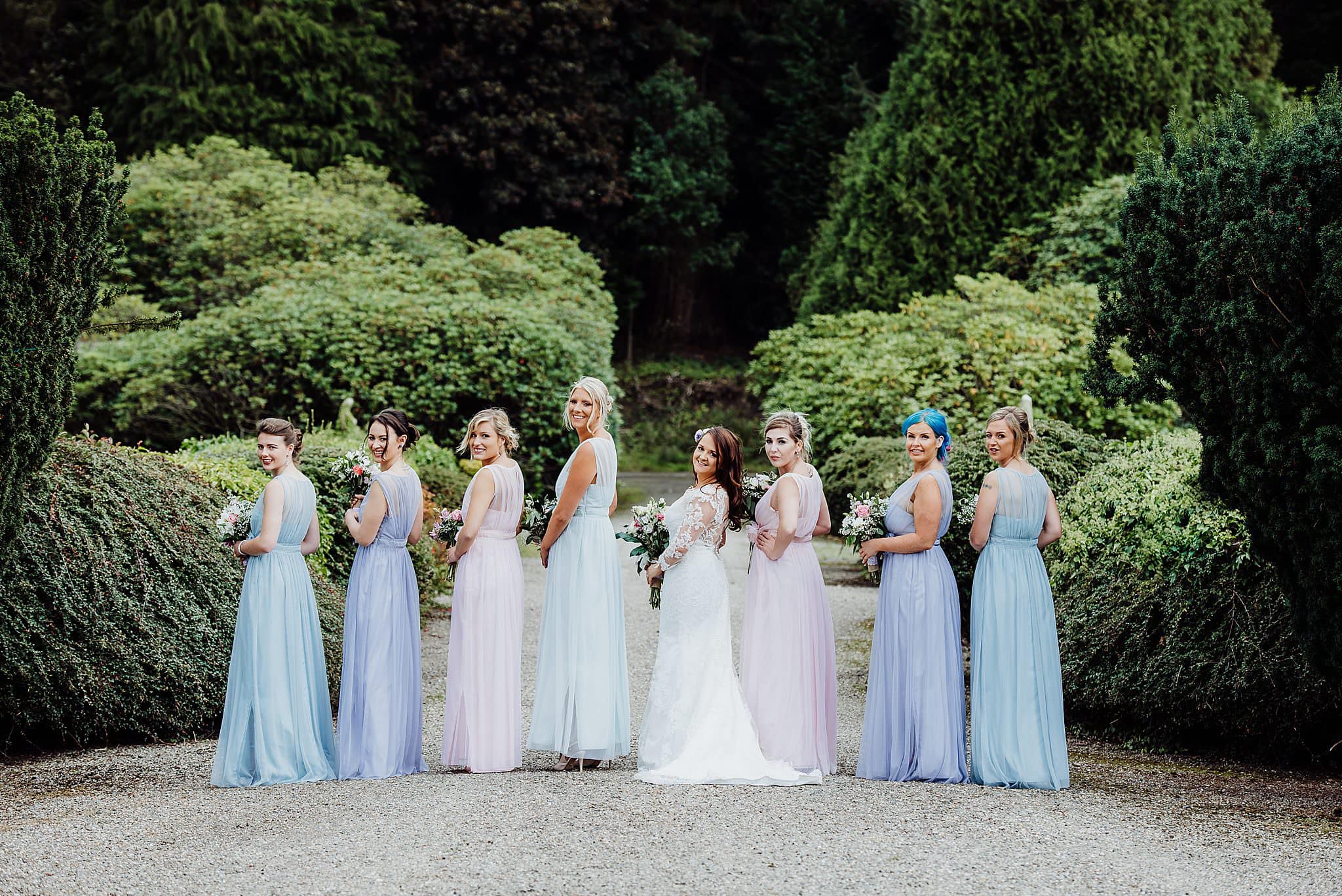 Bride with bridesmaids standing in a line looking back at the camera wearing multi coloured bridesmaids dress at Gregnog Hall wedding venue