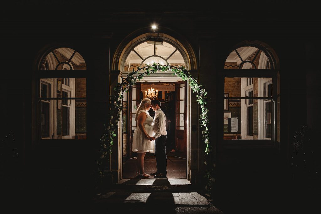 Bride and groom stand nose to nose in the doorway of Court Coleman wedding venue at night being backlit