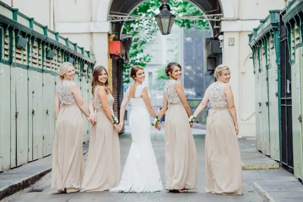 Bridesmaids holding hands walking away with their heads turned back towards the camera