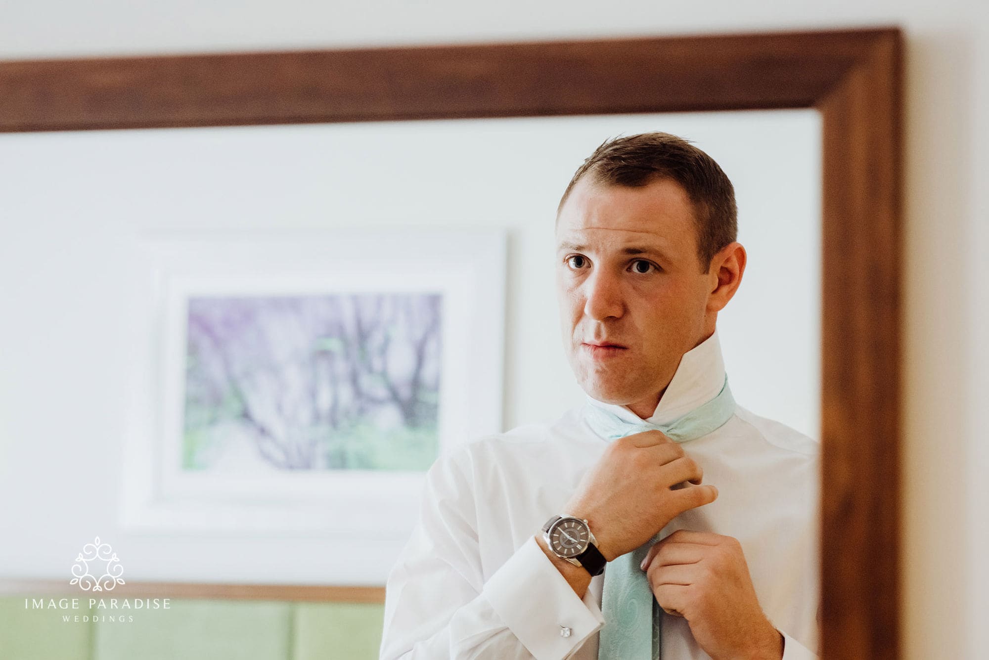 Groom putting tie on in a bedroom of the Cotswolds hotel and spa wedding venue