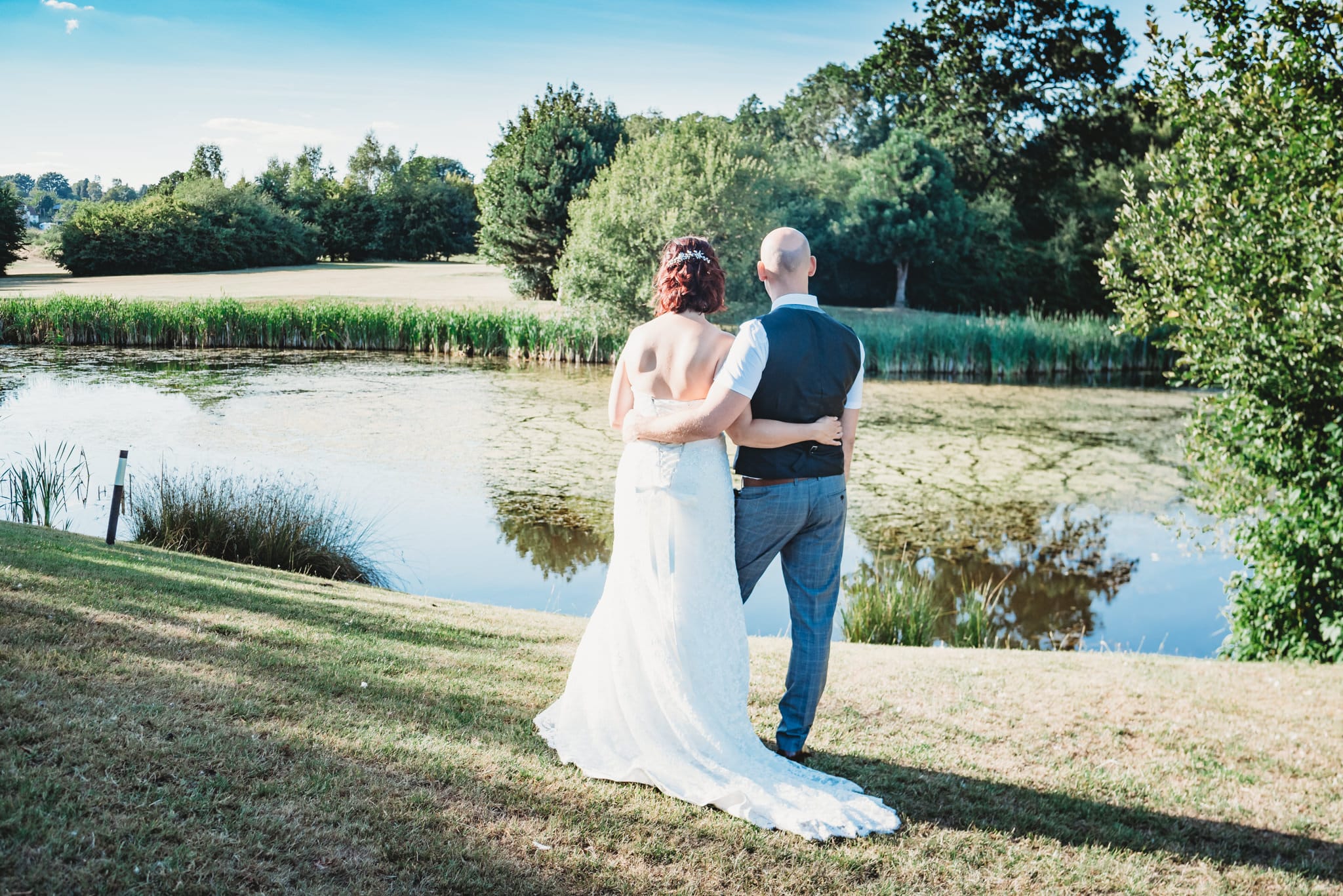 Newly Married couple stood with arms round each other looking at the lake at Kendleshire Golf Course