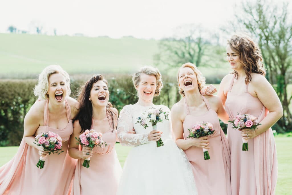 Bridesmaids arm in arm laughing at Priston Mill