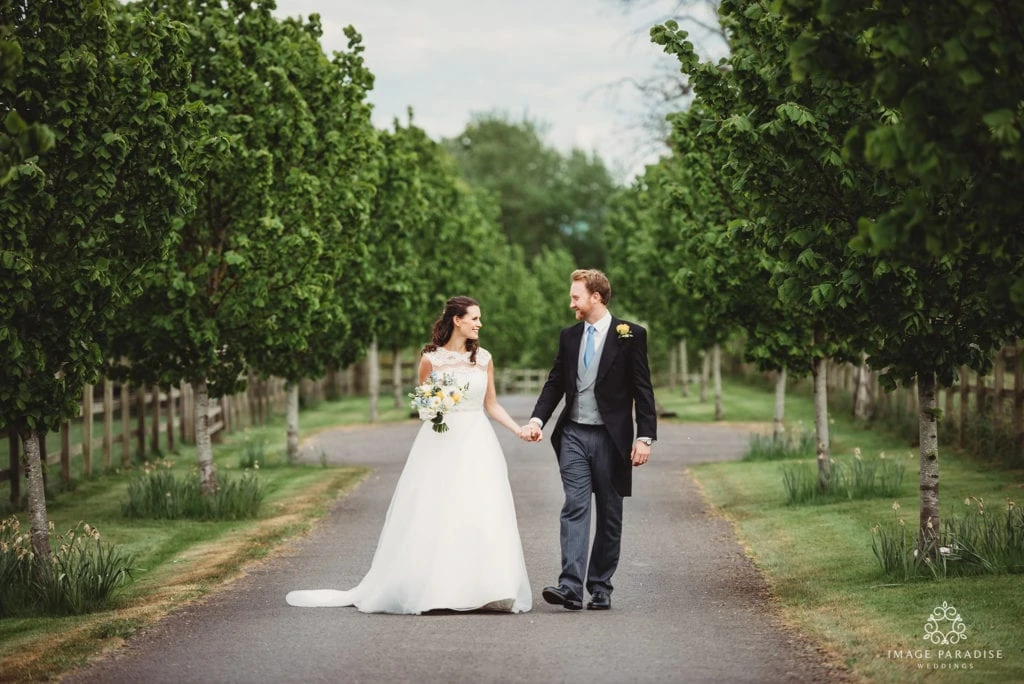 Bride and groom hold hands walking down the tree lined path of Wick Farm Bath wedding photographer